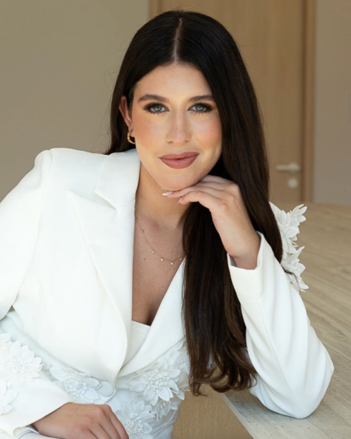 Yuliana Naim in a white suit, seated at a table